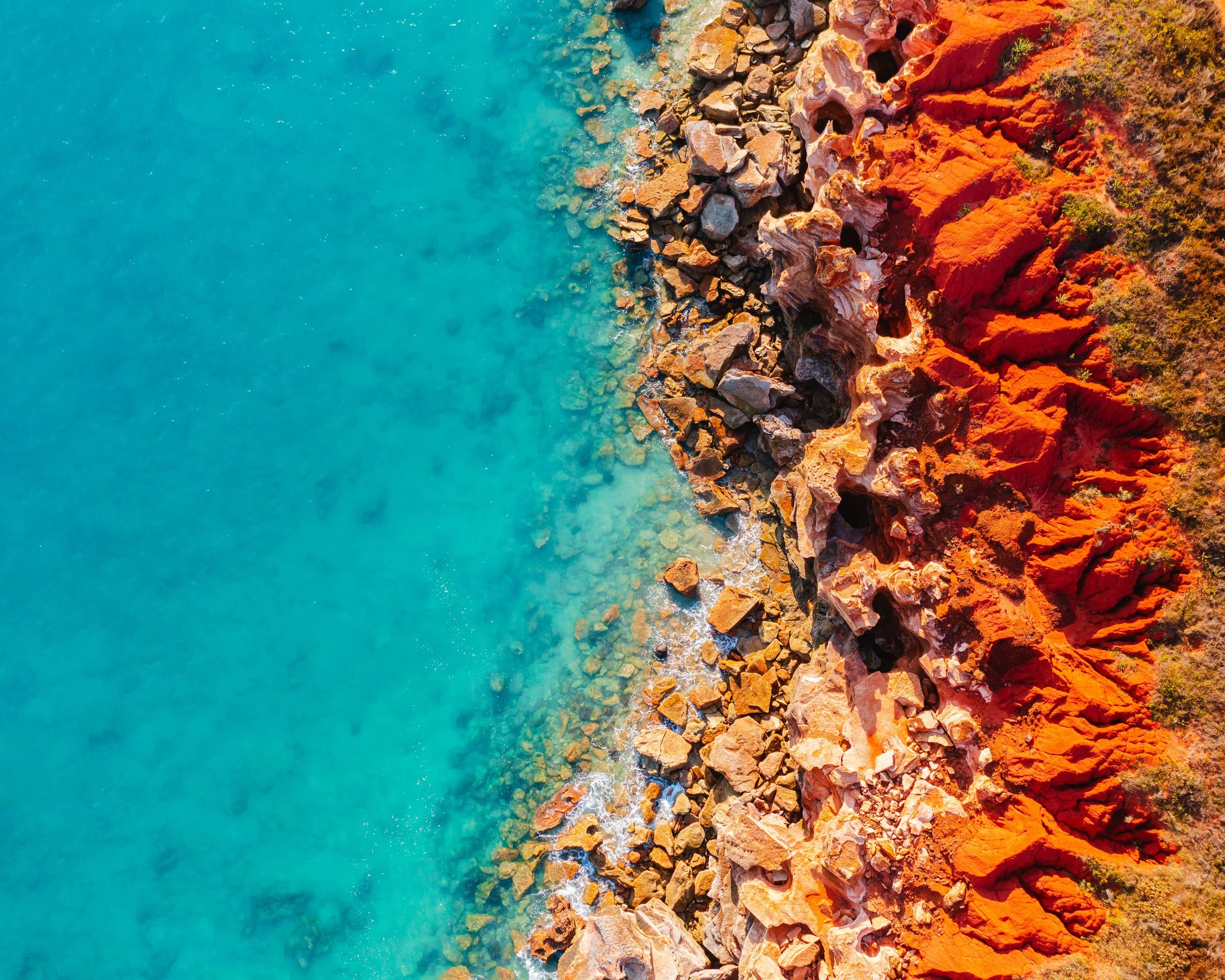 Aerial view of Gantheaume Point in Broome, Australia, showcasing the striking contrast between the turquoise sea and the rich red coastal rock formations.
