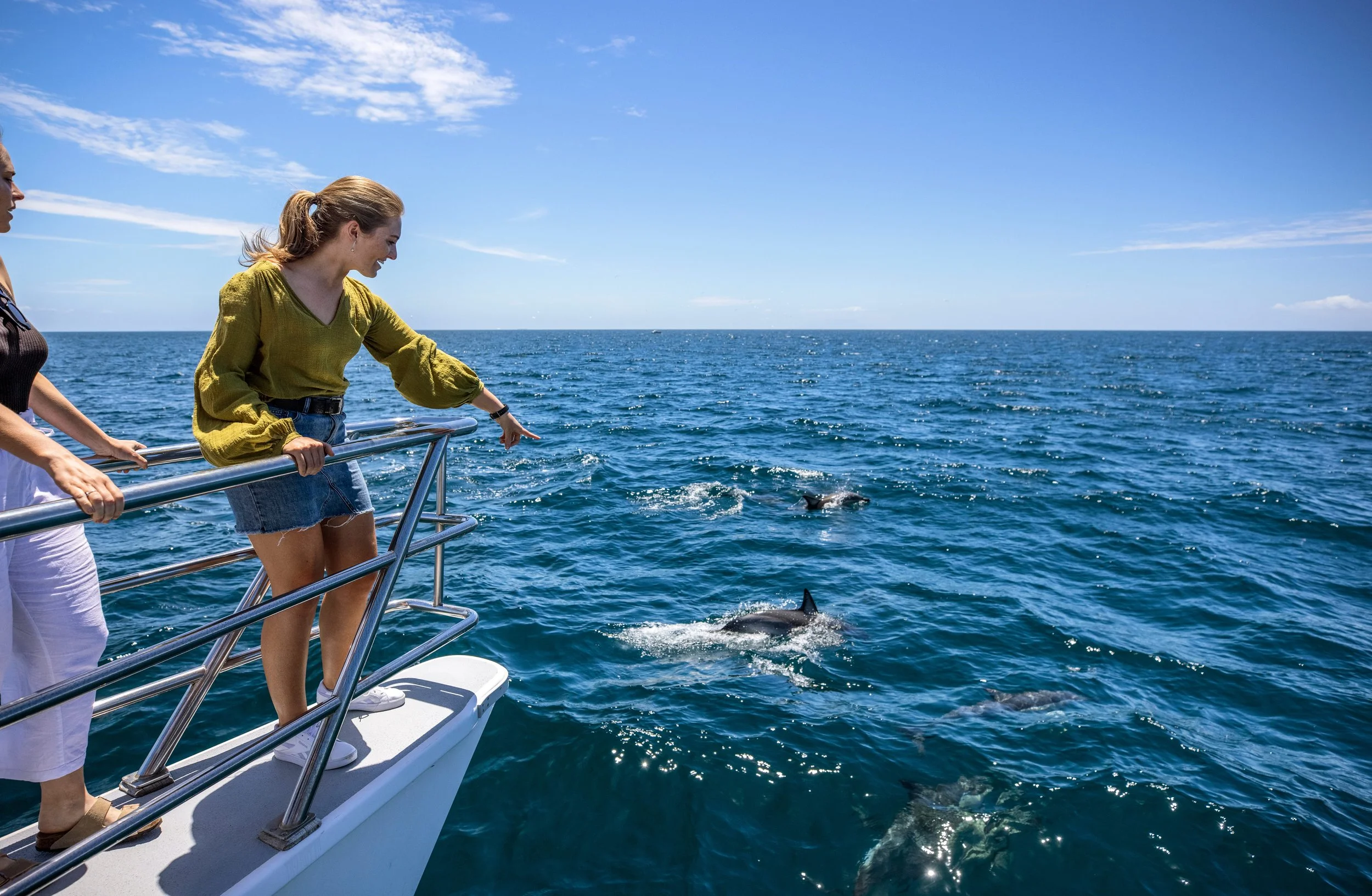 A woman on a boat in the Hauraki Gulf near Auckland, watching whales surface in the sparkling ocean waters around her.