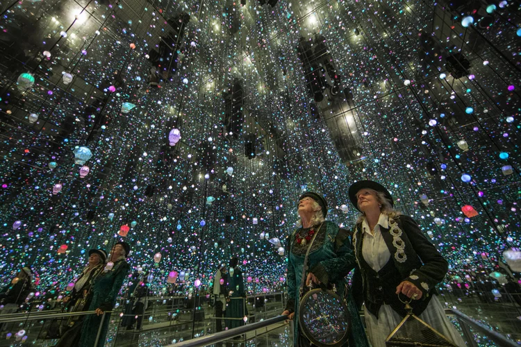 Two senior travellers standing beneath a glowing ceiling of thousands of glowworms inside a New Zealand cave.