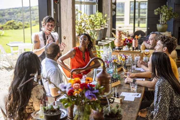 Adults laughing and chatting over a long lunch table set with wine and fresh-cut flowers at a Marlborough vineyard estate.