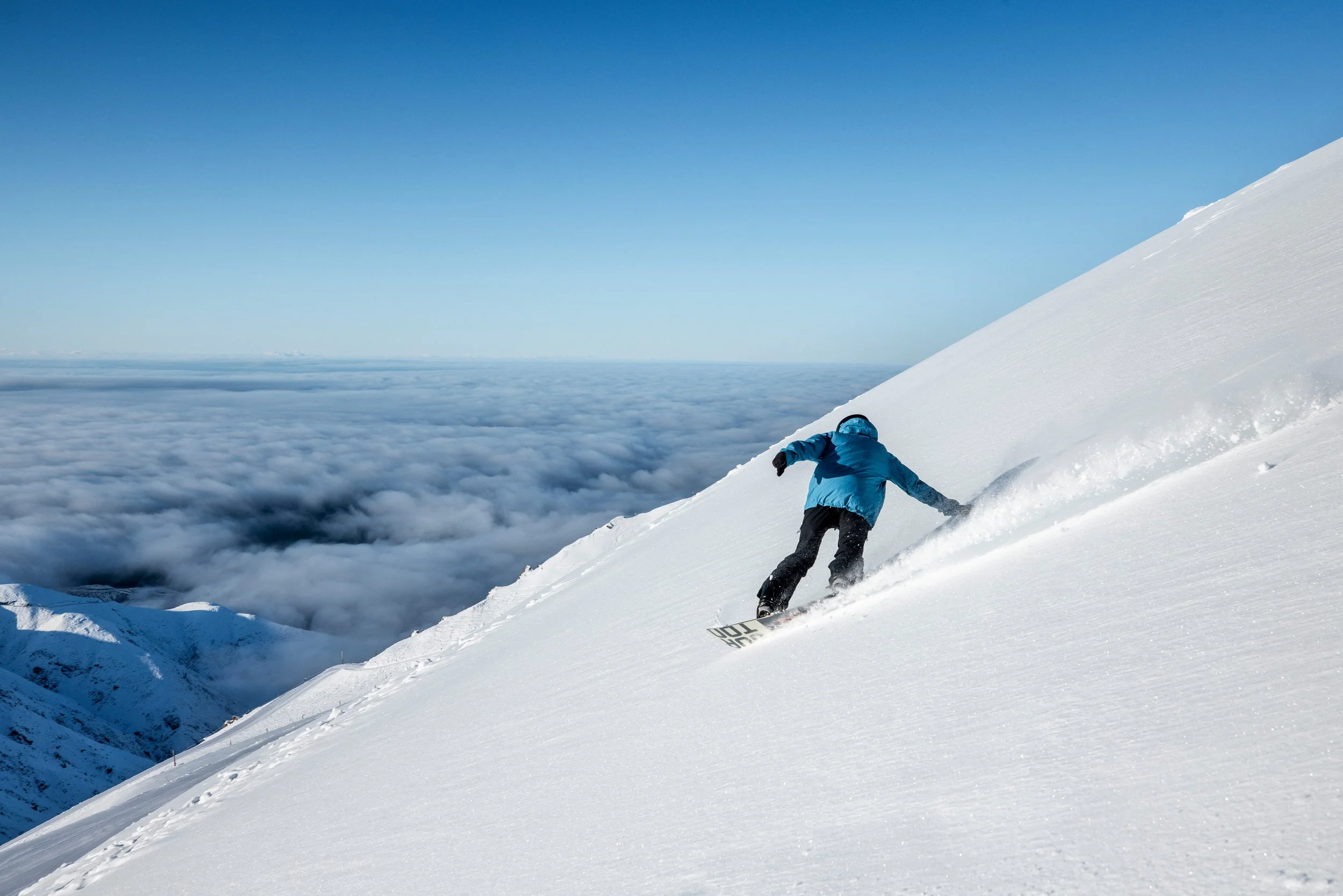 A snowboarder carving through fresh powder on the slopes of Mt Hutt Ski Field during winter, surrounded by snowy mountains and crisp alpine scenery.