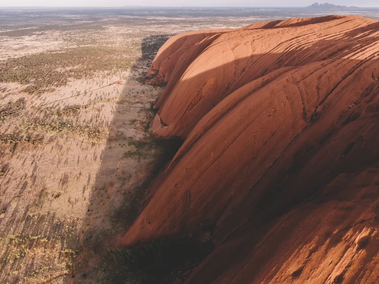 Aerial view of Uluru, also known as Ayers Rock, a large red sandstone formation in Australia, with surrounding desert and sparse vegetation.