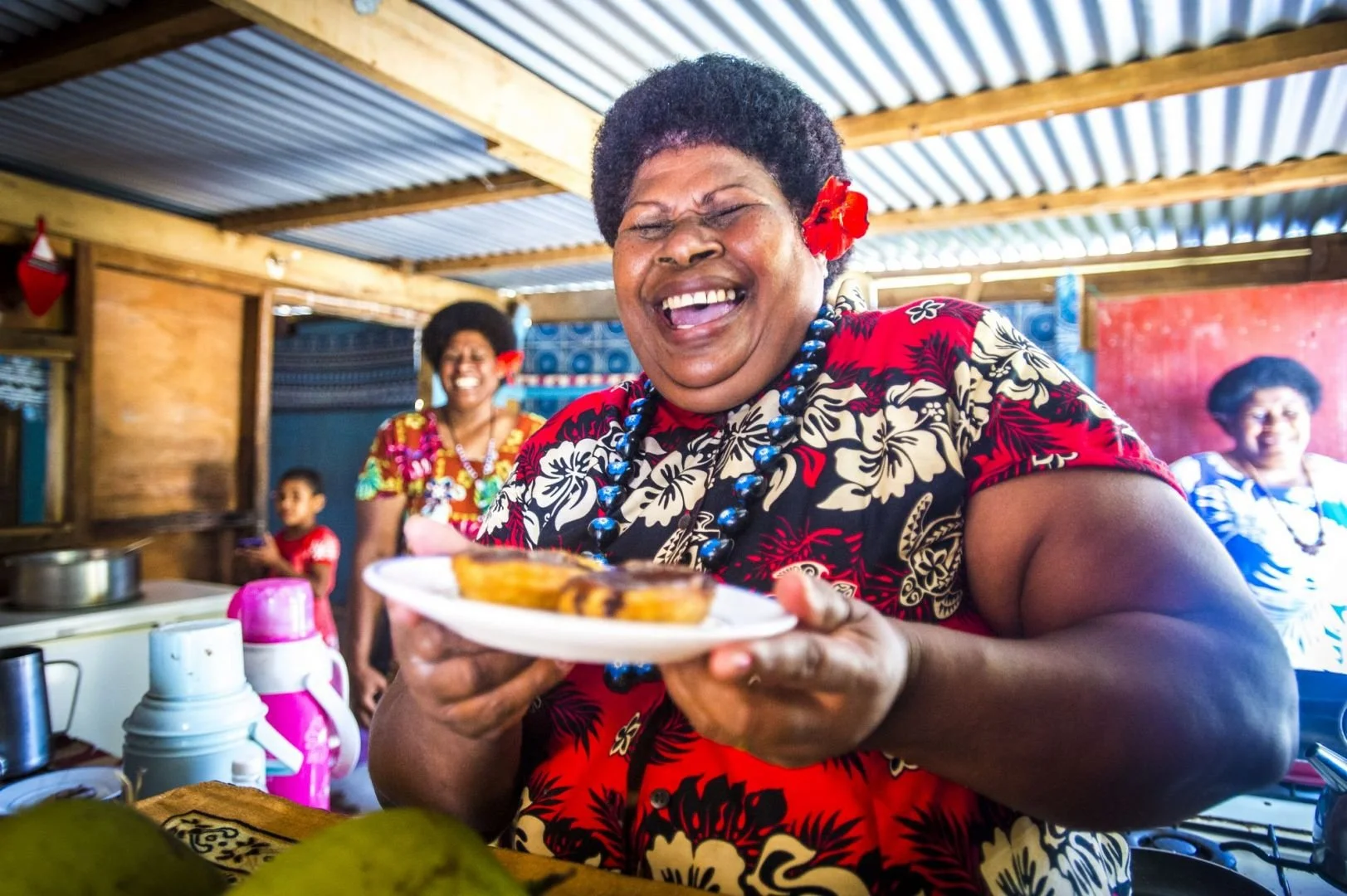 A Fijian woman holds up a plate of food, laughing and smiling
