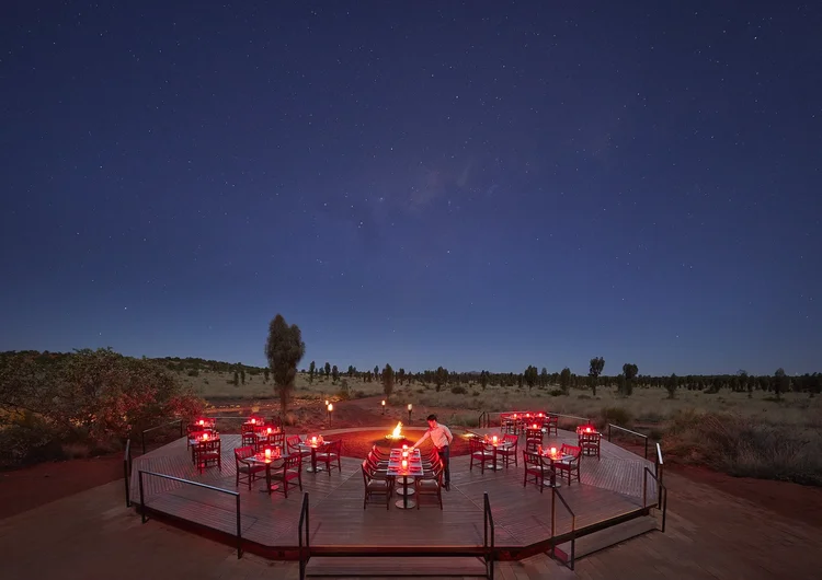 A luxurious private dining experience at Longitude 131° in Uluru, Australia, with an elegantly set table under the stars, hosted in the open outback and framed by views of the iconic Ayers Rock.