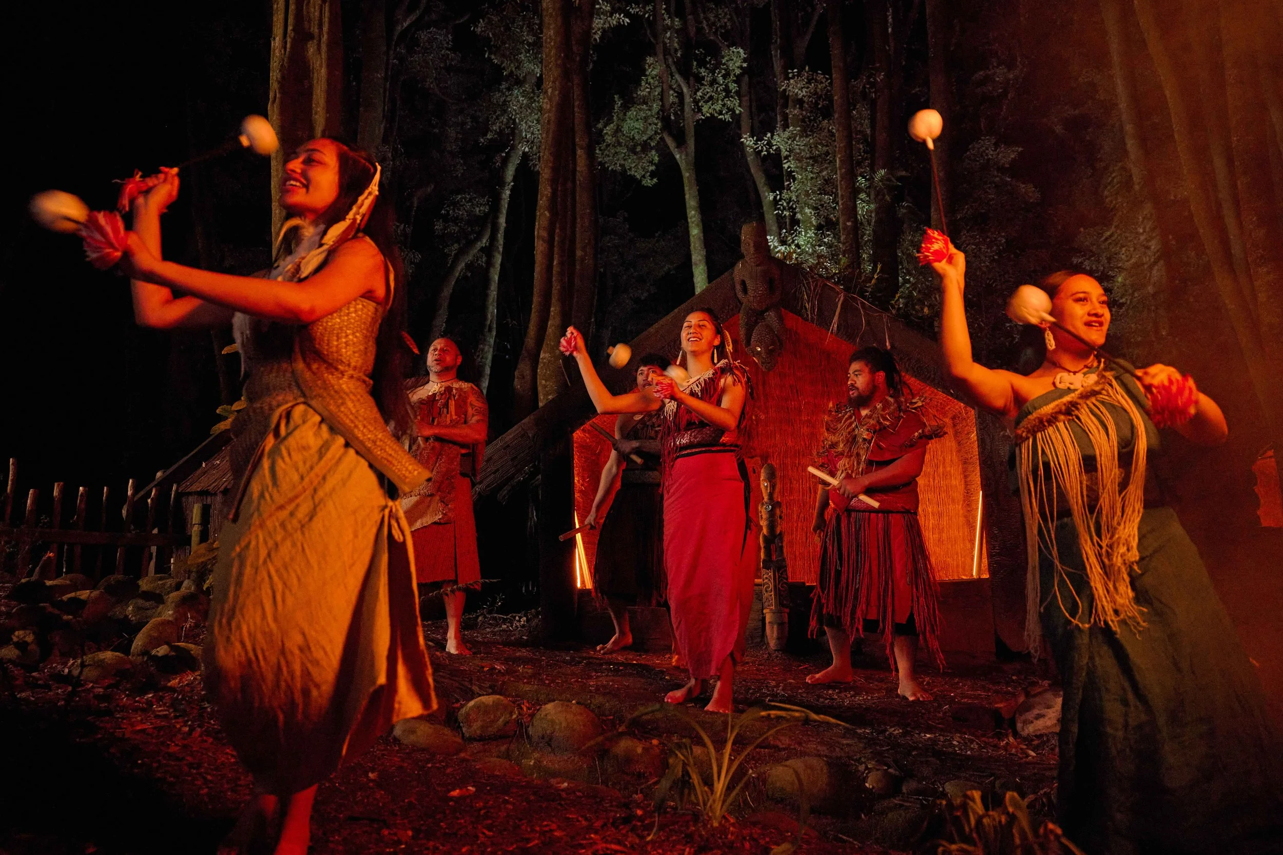 Māori performers in traditional dress swing poi by firelight during an evening cultural performance beside a marae, New Zealand.