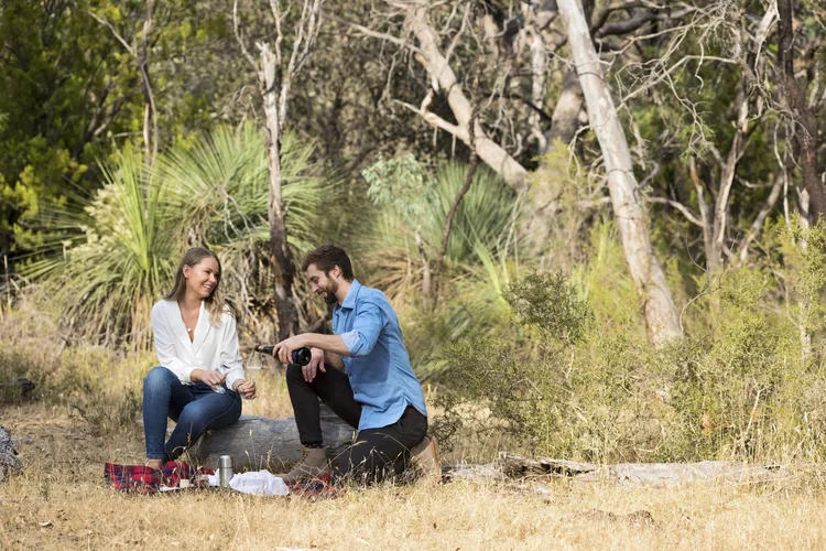 A couple enjoys a private wine tasting picnic in Barossa Valley, Australia, surrounded by tall trees, dappled sunlight, and the peaceful sounds of nature.