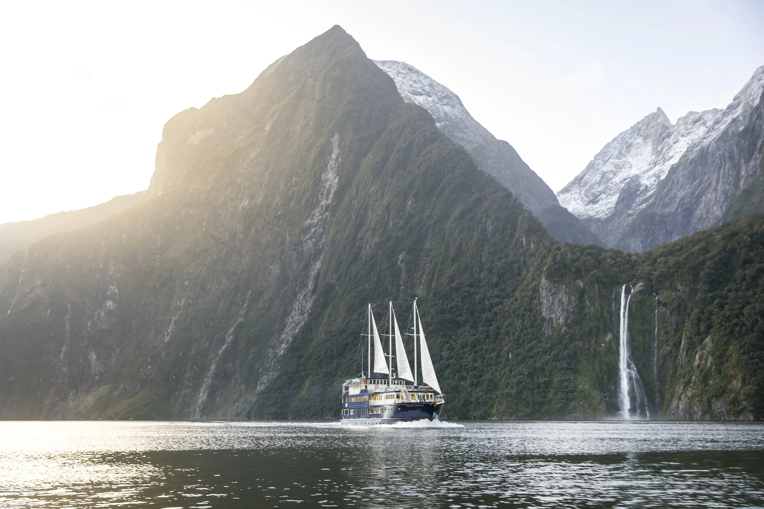 View of a boat set against the towering cliffs, glaciers, and waterfalls of the Milford Sounds in New Zealand