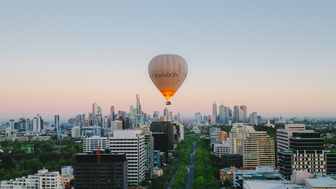 A CHANDON hot air balloon floats over a city skyline at dusk, with high-rises, a green park, and a pink-blue gradient sky in the background.