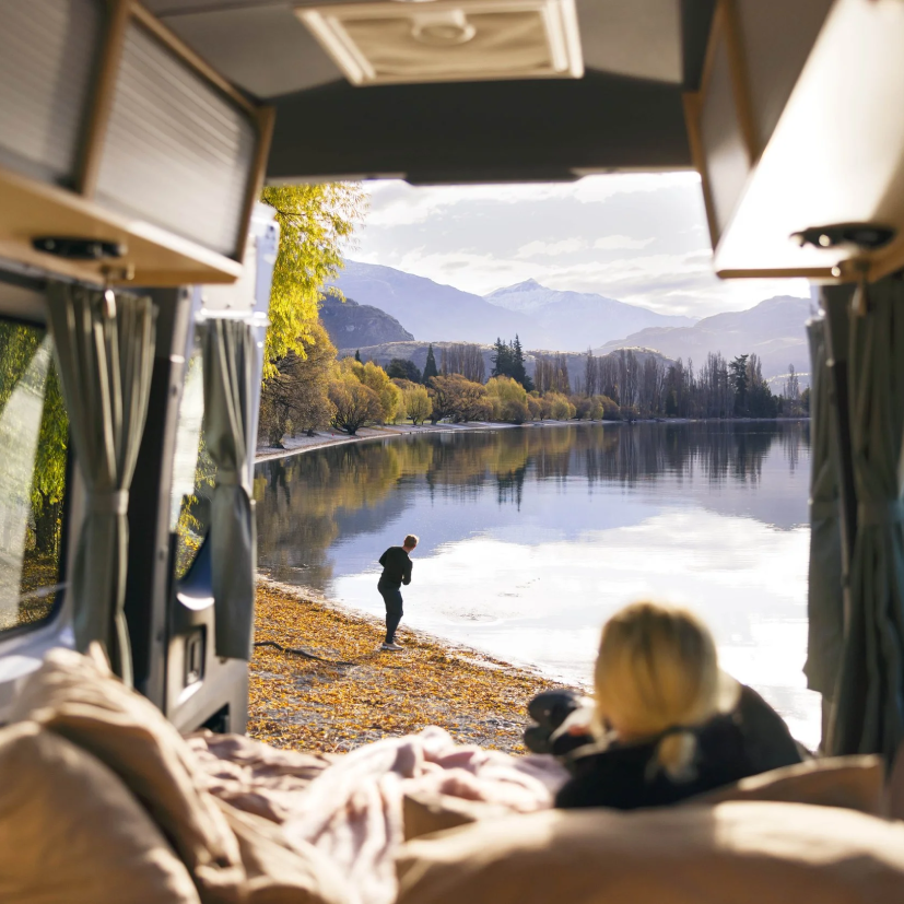 A couple relaxing inside a campervan overlooking a mountain lake in New Zealand.