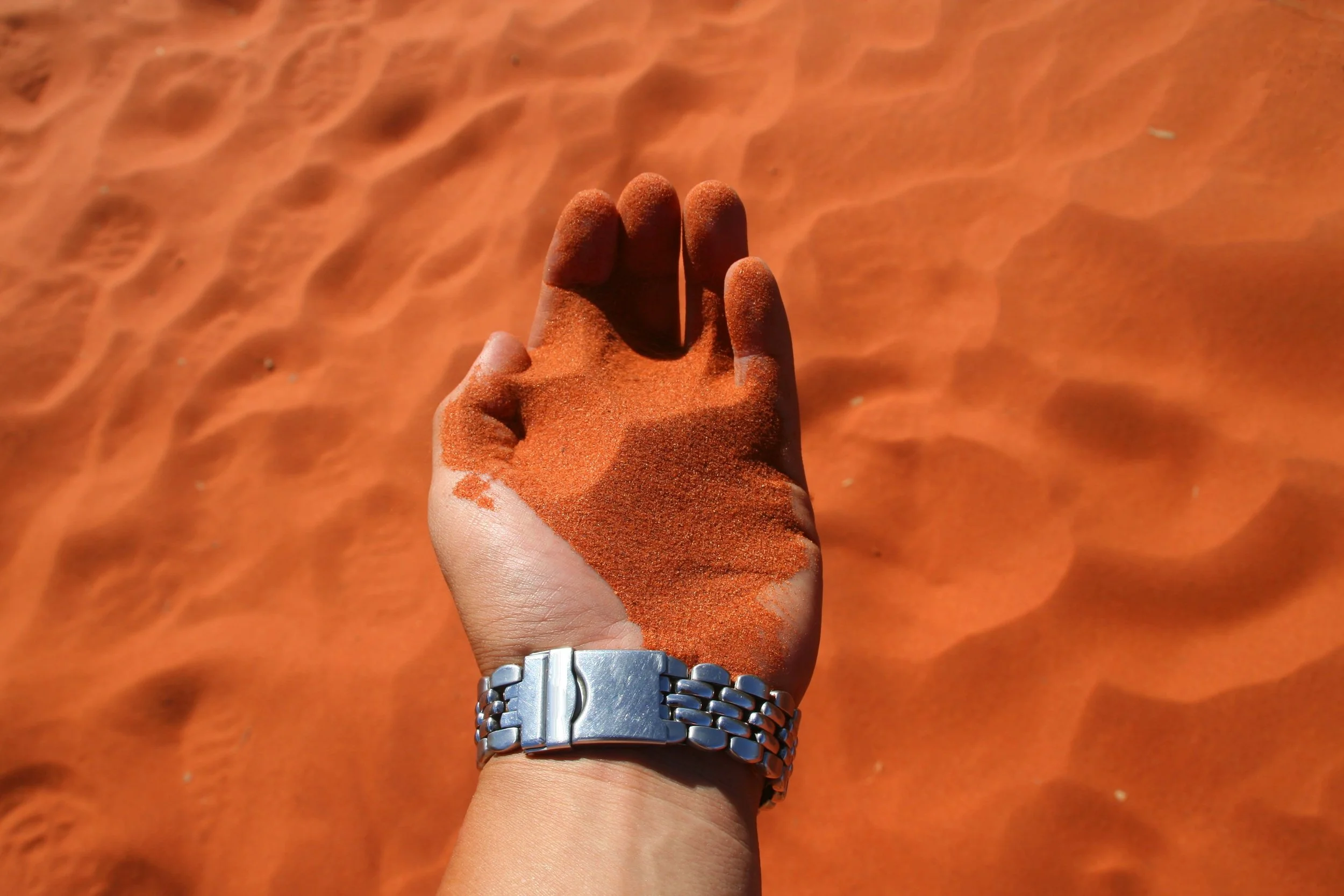 A person’s hand picking up the red sand of Uluru in central Australia.