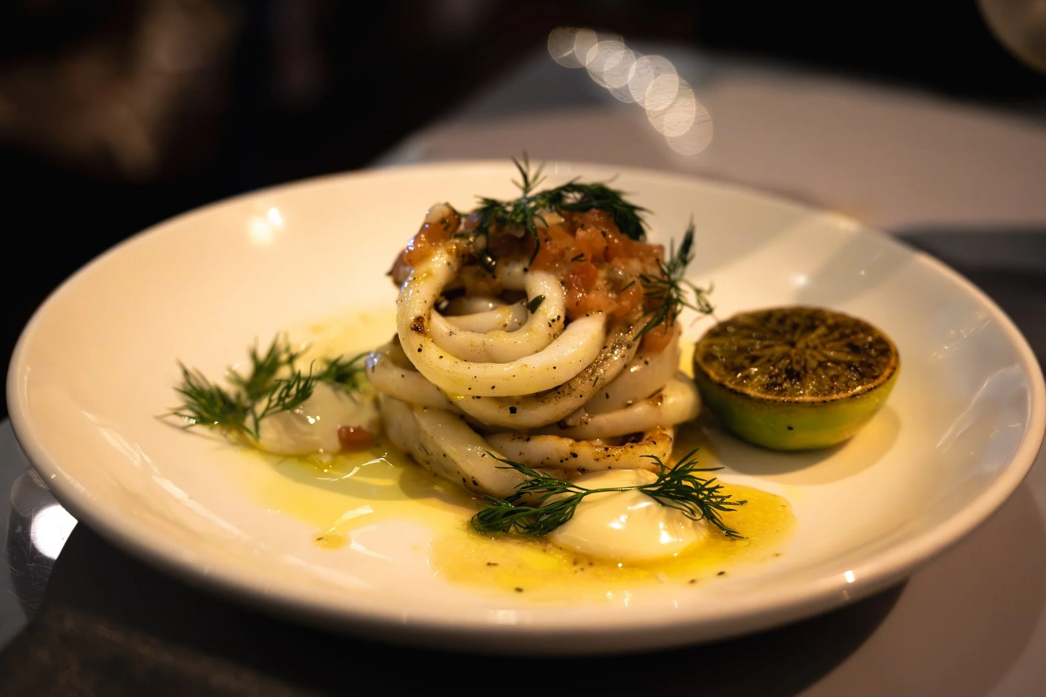 Grilled calamari topped with tomato salsa in plate and fresh lime on side in a fine-dining restraurant in Melbourne, Australia.
