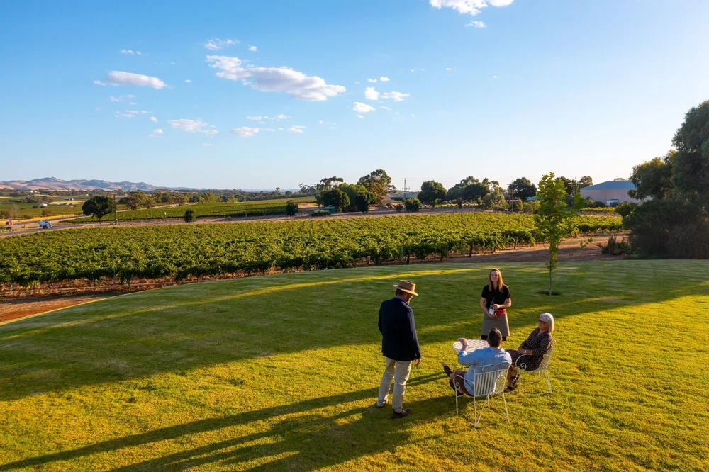 A couple seated at an outdoor table at a winery in Adelaide, Australia, smiling and enjoying a private wine tasting with glasses of red and white wine, surrounded by vineyard views and natural scenery.