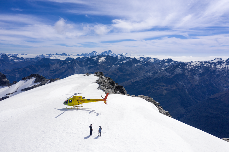 A helicopter and two people standing on a snow-covered alpine ridge in New Zealand’s Southern Alps.