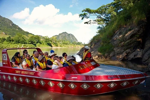 Group of tourists on a red speedboat on a river surrounded by green trees and mountains.
