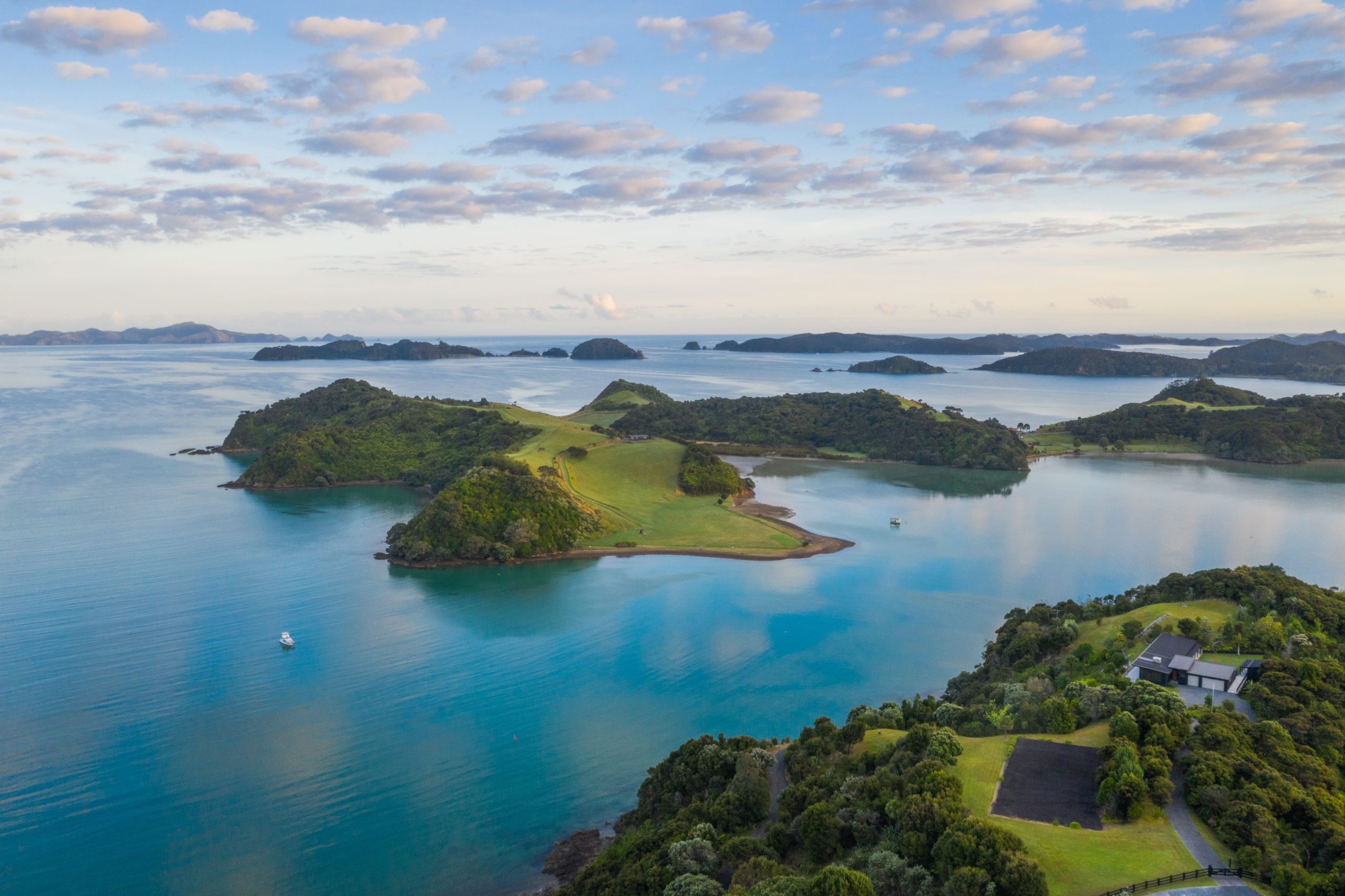 Aerial view of Paroa Bay, located in the heart of the Bay of Islands, NZ. The sky reflects off the bright blue sea.