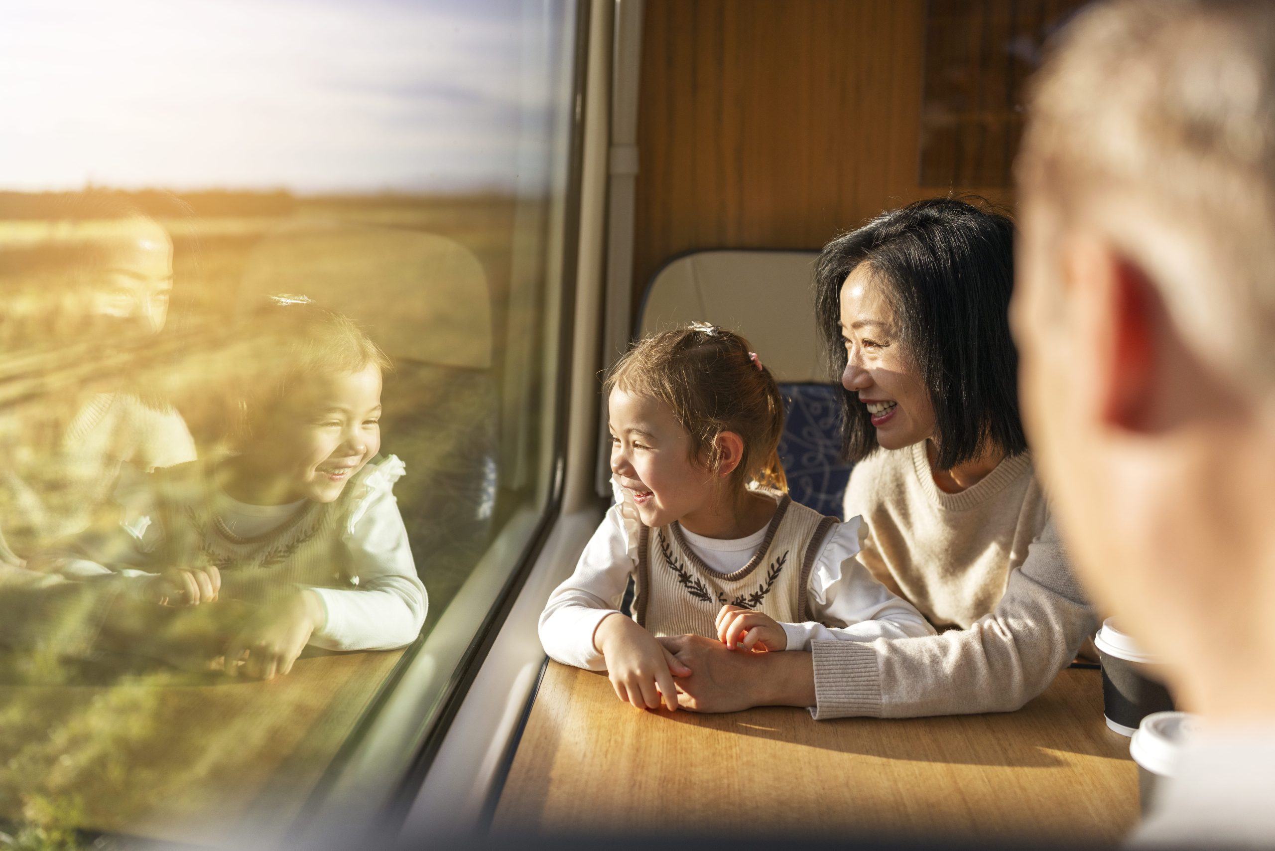 Mother and daughter enjoy scenic train ride from Christchurch to Greymouth. They are both looking out the window and smiling.