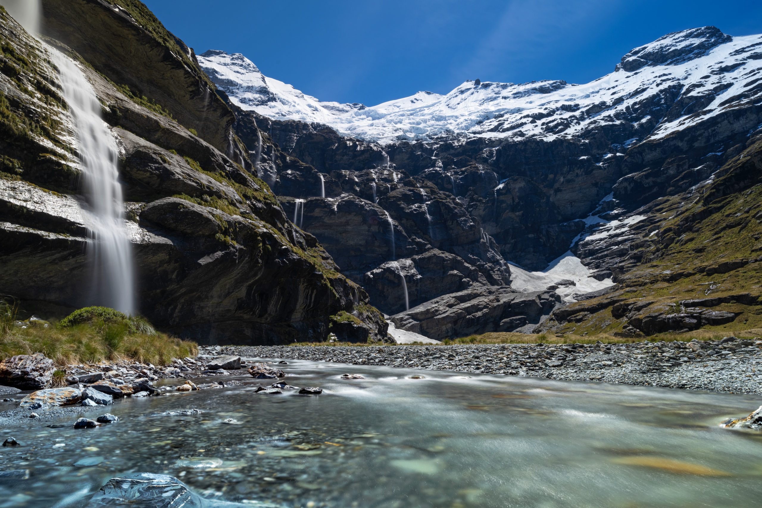 Wide shot of dramatic glacier valley at Earnslaw Burn, New Zealand, featuring a massive, dark rock amphitheater under a snow-covered hanging glacier
