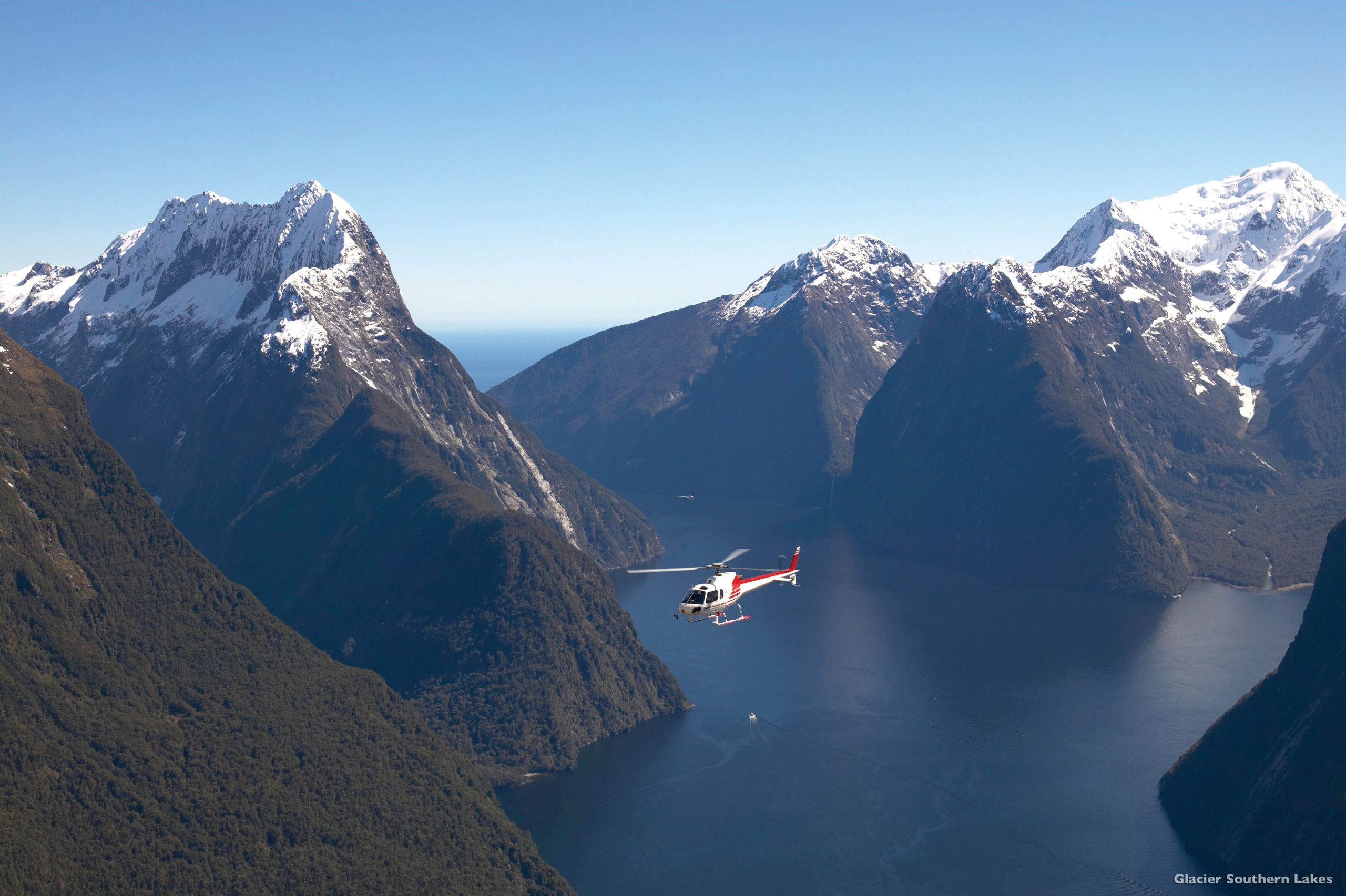 A helicopter hovers over dramatic landscape of Milford Sound, New Zealand.