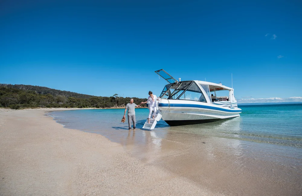 A senior couple steps off a private charter boat tour onto a white sandy beach