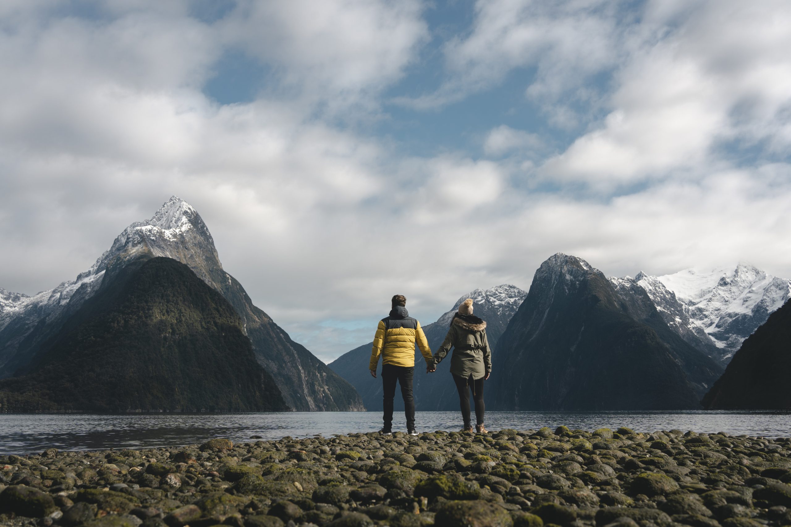 Couple holding hands at the majestic landscape of fjords in Milford Sound. Fiordland, New Zealand