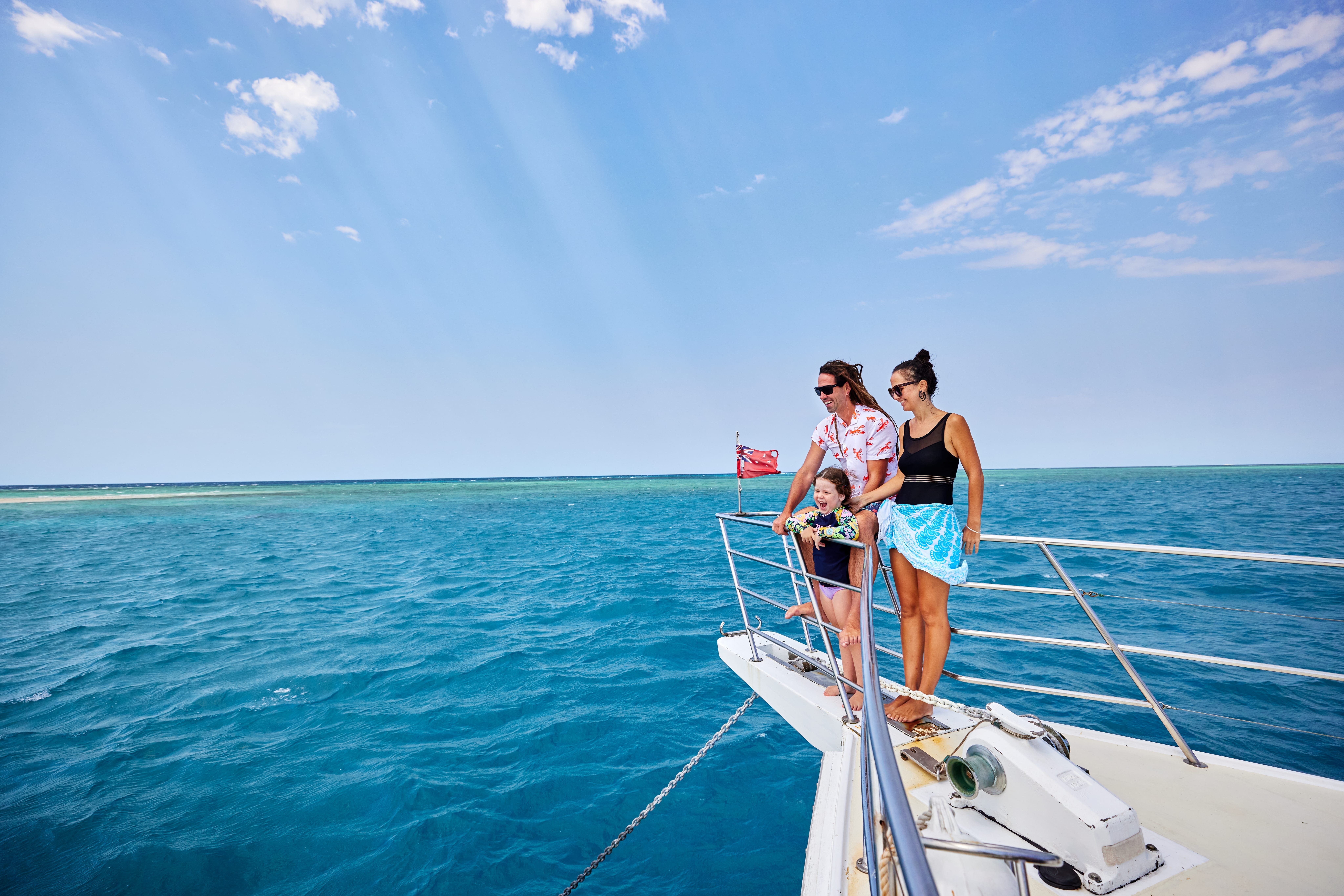 Two parents and their young child look over the stern of a private charter boat, exploring the Great Barrier Reef.
