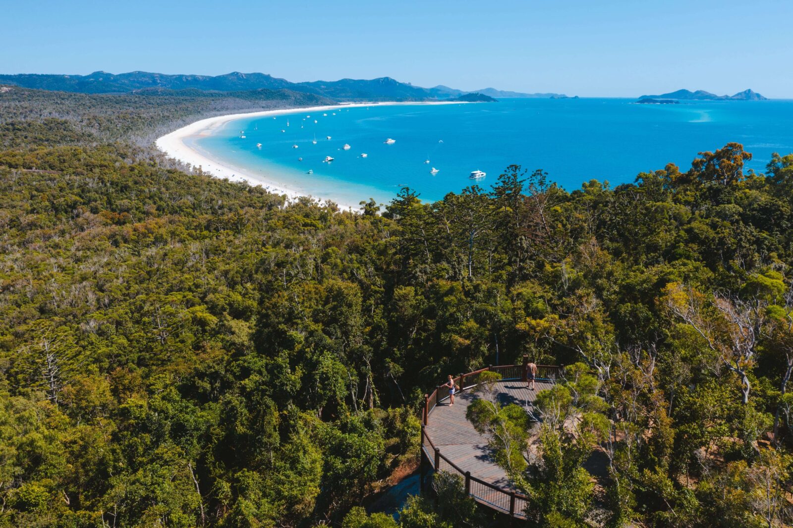 Aerial view of Whitehaven Beach’s swirling white sand and turquoise water at Hill Inlet, with a forested lookout boardwalk in the foreground.