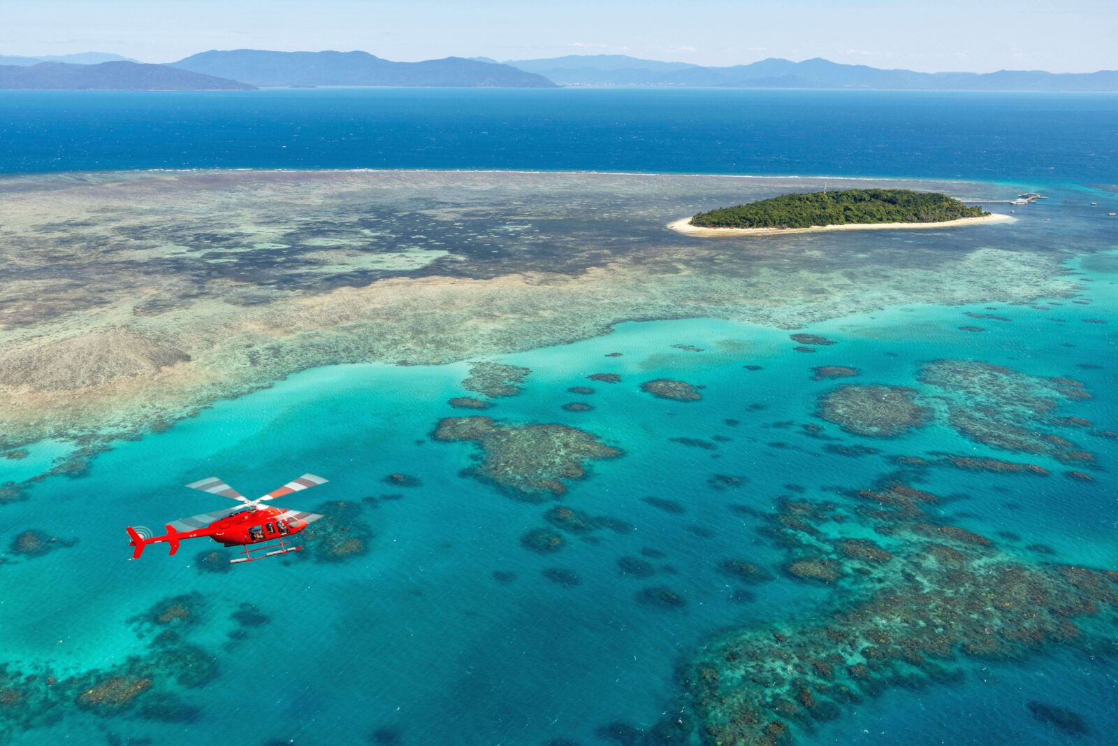 A helicopter flies low over turquoise water on the way to Green Island, Great Barrier Reef.