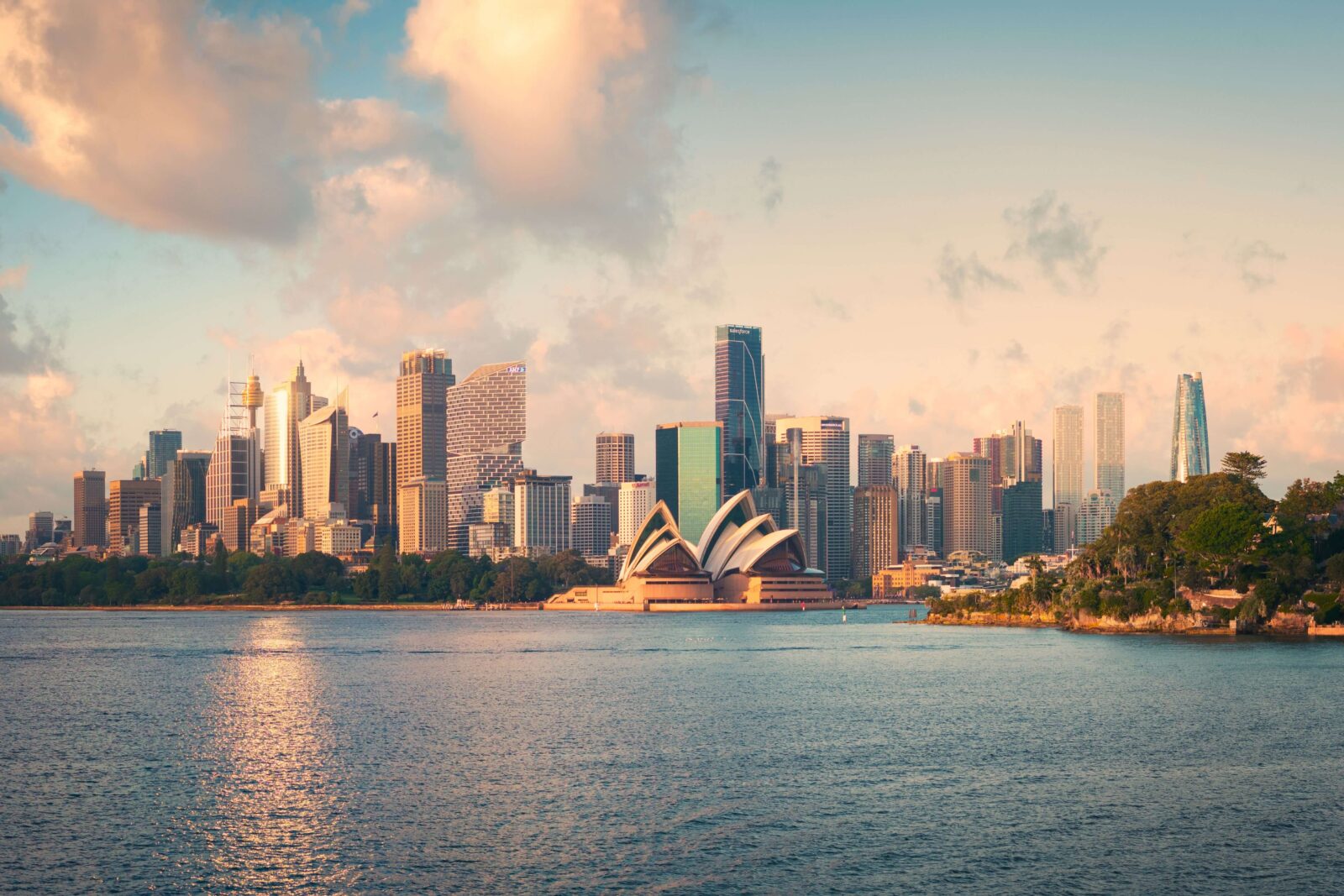 Sydney’s skyline and harbour at dusk, with the Sydney Opera House in the foreground and city towers silhouetted against a warm, cloudy sky.