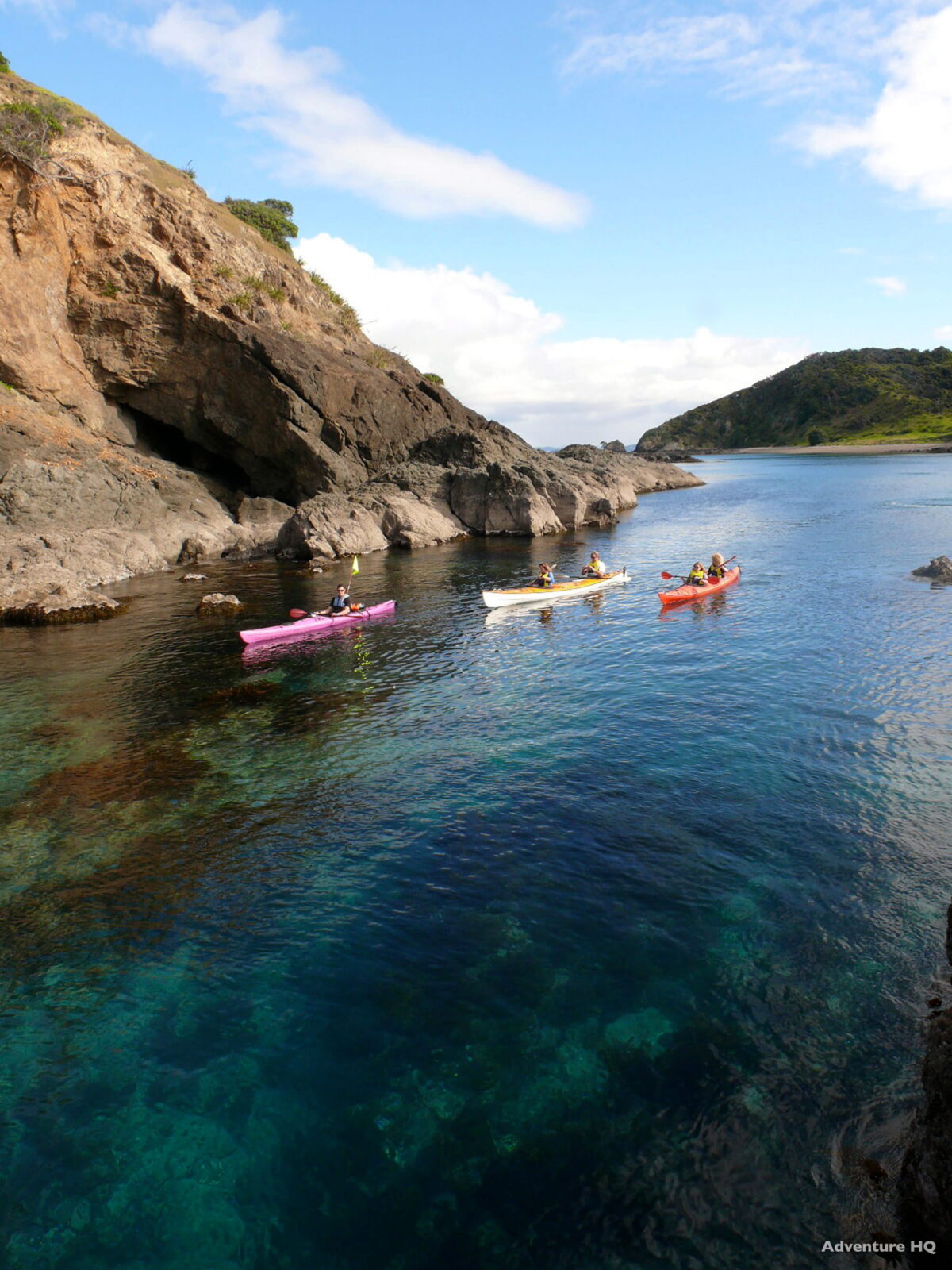 Sea kayakers paddling calm turquoise water through a narrow, cliff-lined rocky cove near the Bay of Islands.