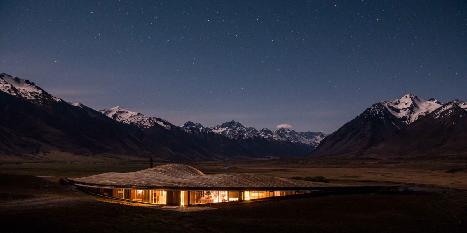The Lindis Lodge, a luxury 5-star hotel, sits against a stunning backdrop of snow-capped mountains at dusk.