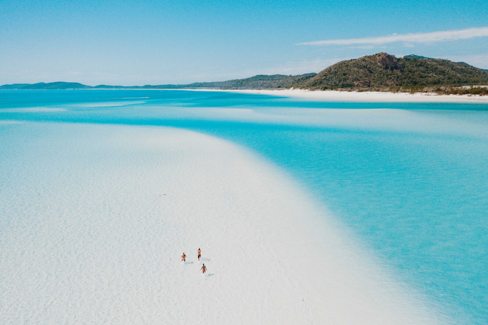 Aerial view of turquoise water meeting white sand at a beach, with two people walking along the shoreline