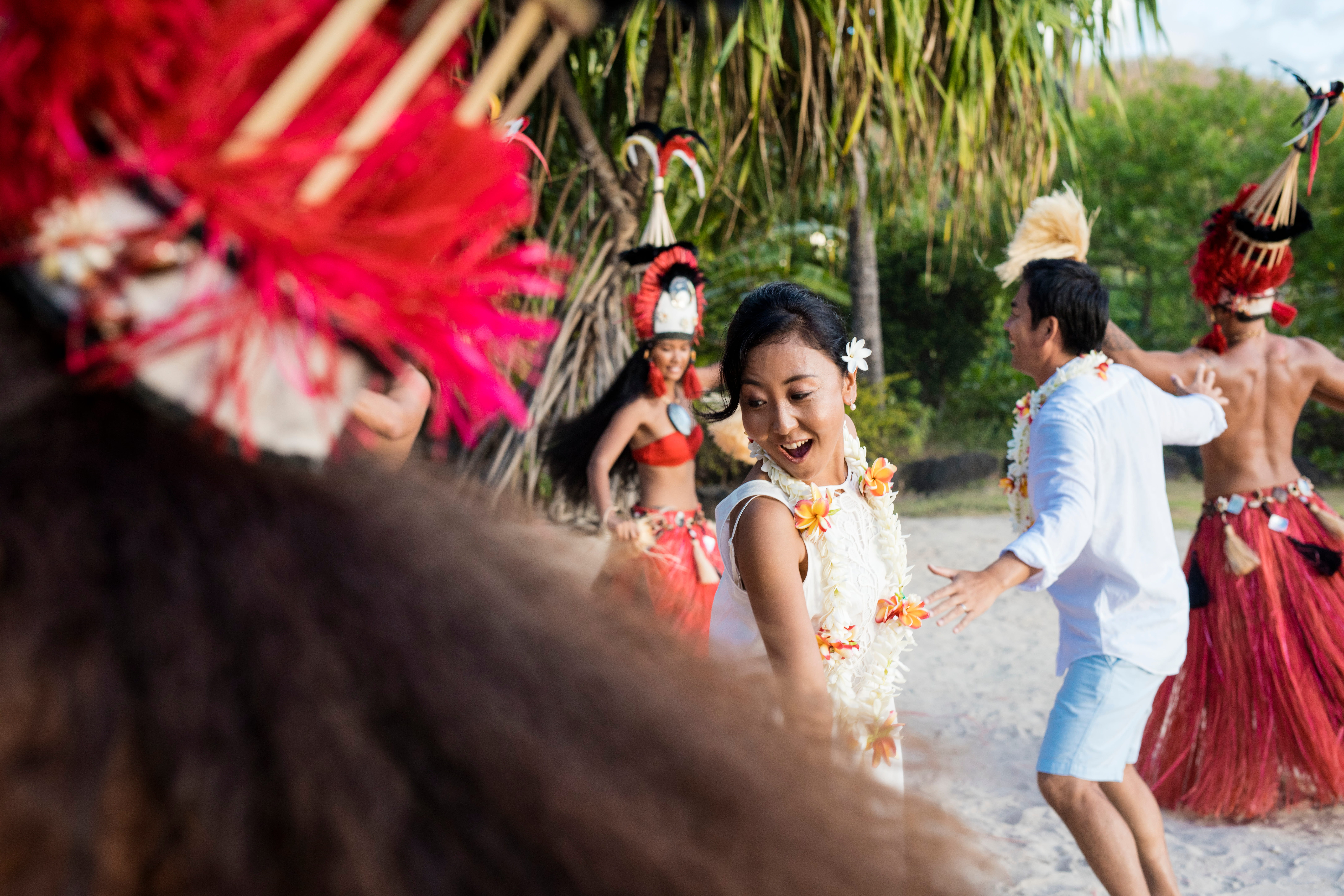 A couple being welcomed with leis by traditional Fijian dancers on the beach.