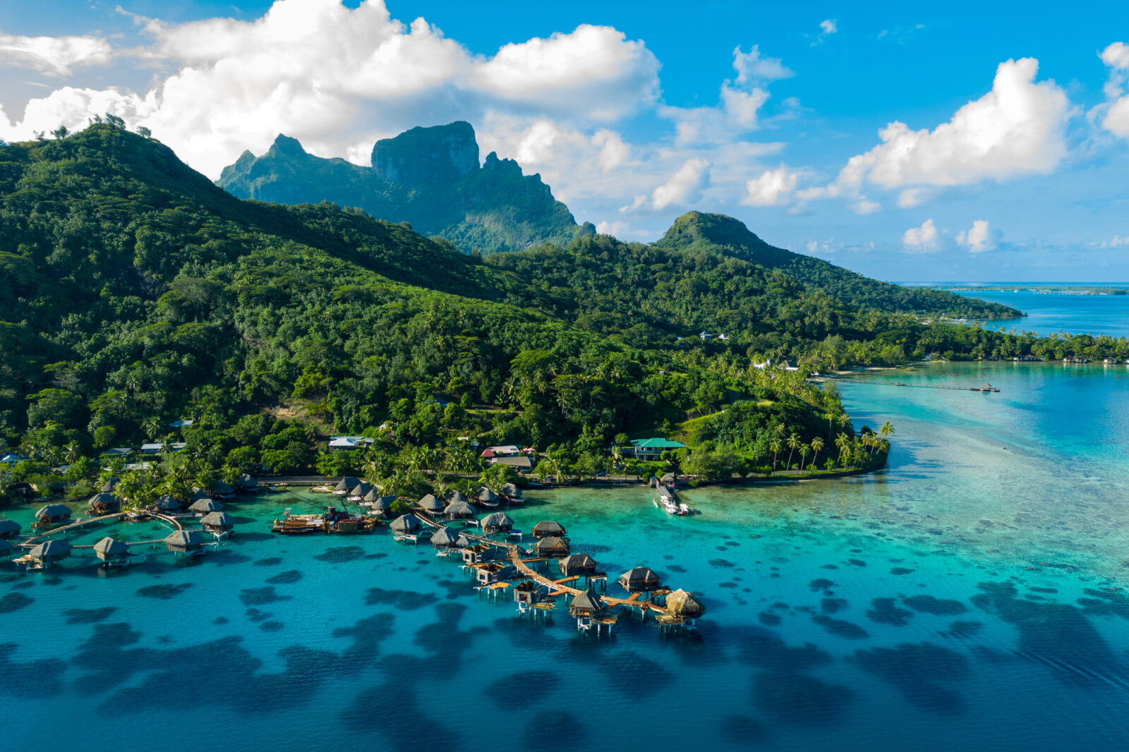Aerial drone shot of Bora Bora featuring overwater bungalows, coral reefs, and a stunning coastline.