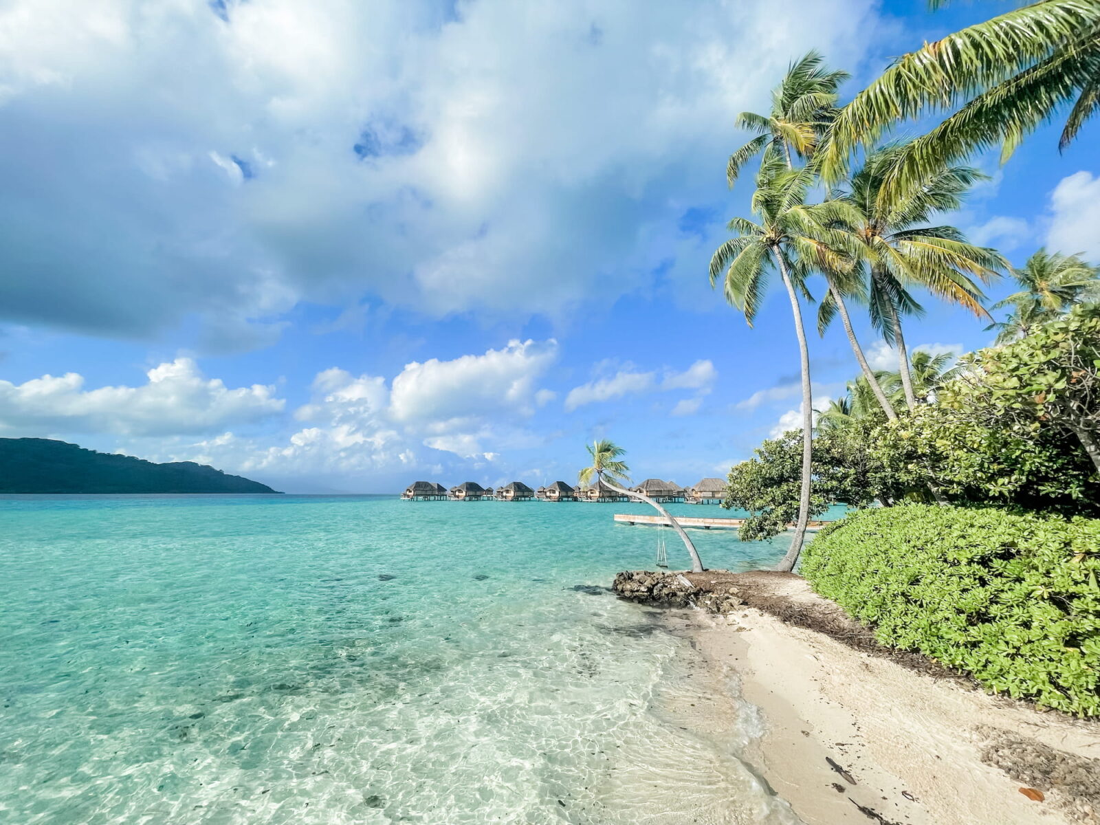 Turquoise lagoon and coastline, Taha’a Island, Tahiti. Overwater bungalows can be seen in the distance.
