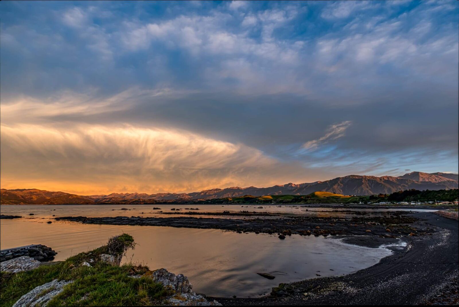 A dramatic and peaceful sunset illuminates the Seaward Kaikōura Range mountains along the coast of Kaikōura, South Island, New Zealand. 