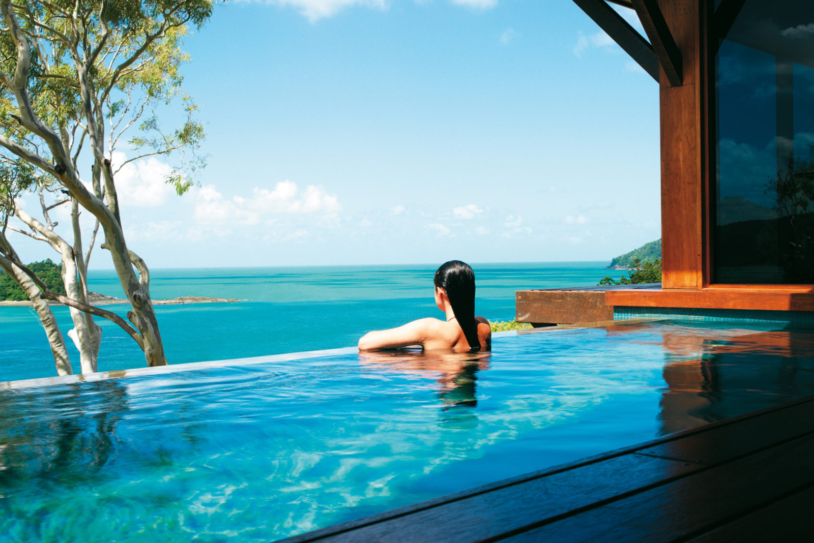 Woman relaxing in an infinity pool overlooking the ocean from a timber lodge